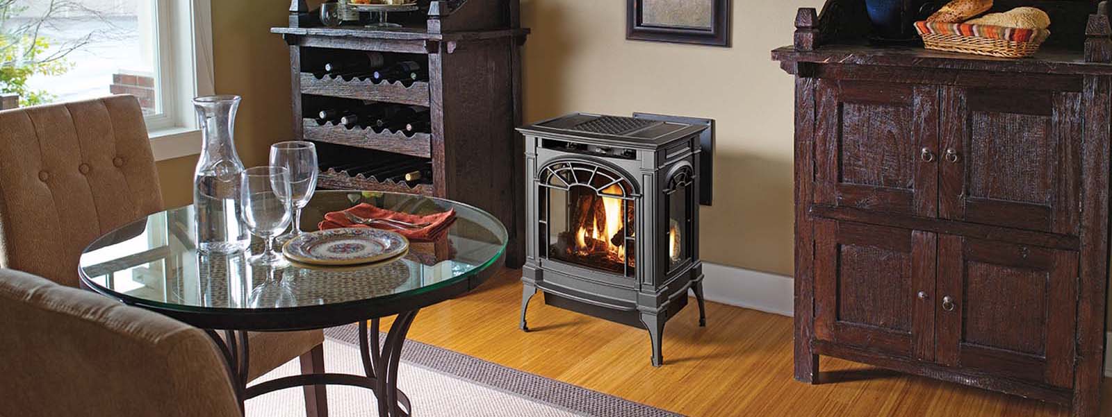 Cozy living room with a freestanding metal wood stove burning beside a glass dining table set with plates and wine glasses.